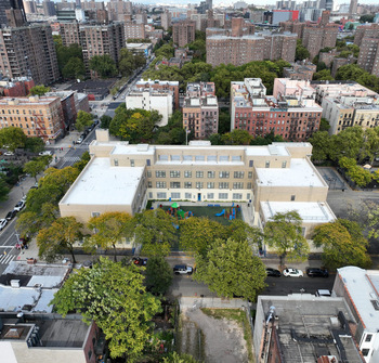 Aerial view of the P.S. 133 building among the apartment blocks and trees of Central Harlem.