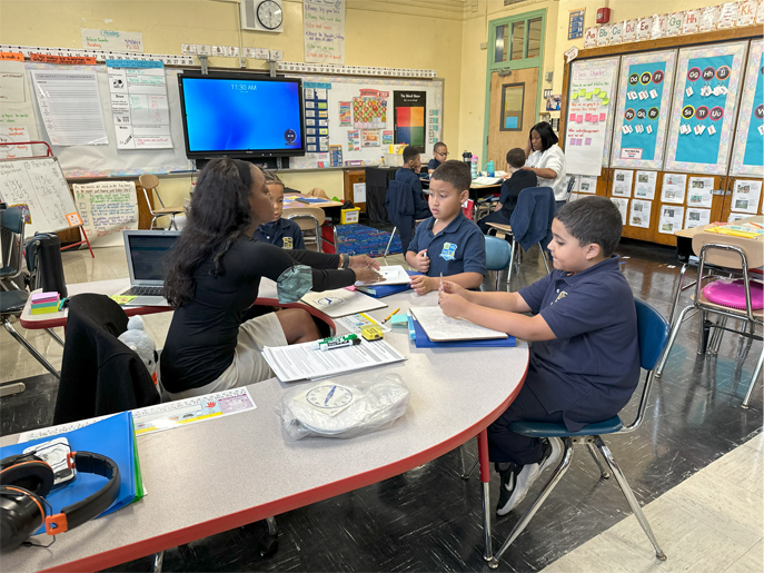 Students work together with their teacher at a curved classroom table.