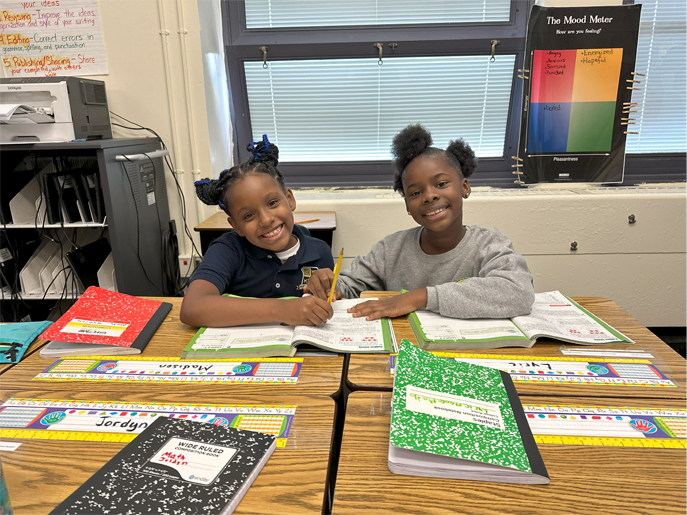 Two students smile while working in their math workbooks.