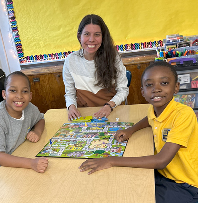 A teacher and two smiling students play a board game together.
