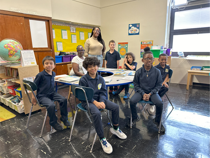 A class seated around a table with their teachers, smiling at the camera.